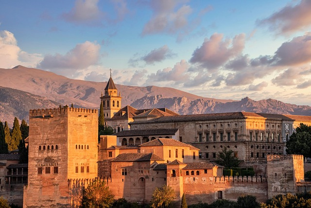 Alhambra in Granada bei Sonnenuntergang, historische Palastanlage mit Türmen und maurischer Architektur vor der Kulisse der Sierra Nevada.