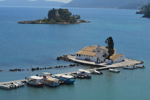 Vlacherna‑Kloster auf Korfu mit weißen Mauern und Bootssteg im türkisblauen Meer, im Hintergrund die kleine Insel Pontikonisi – klassisches Motiv der griechischen Insel.