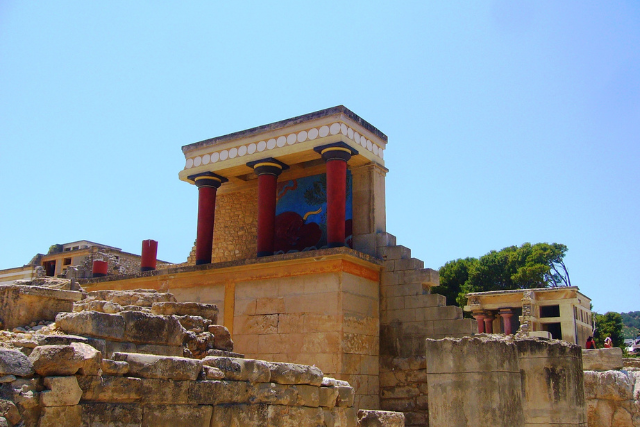 Palast von Knossos auf Kreta mit roten Säulen und antiken Steinmauern unter blauem Himmel – bedeutendes Relikt der minoischen Zivilisation.