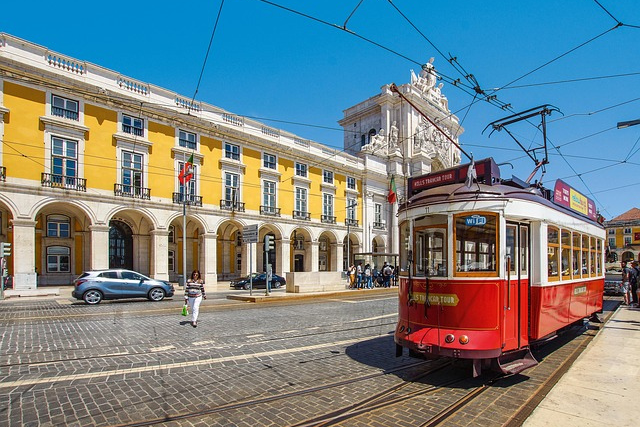 Rote Straßenbahn fährt über die Praça do Comércio in Lissabon, umgeben von gelben Gebäuden und blauem Himmel – Symbol für die lebendige Hauptstadt Portugals.