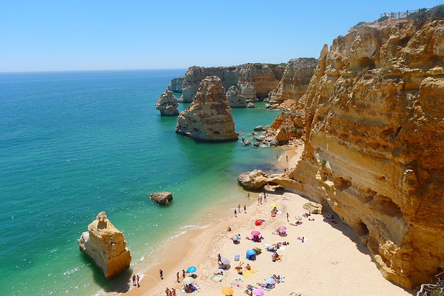 Felsenküste der Algarve mit türkisblauem Meer und goldenem Sandstrand bei Sonnenschein