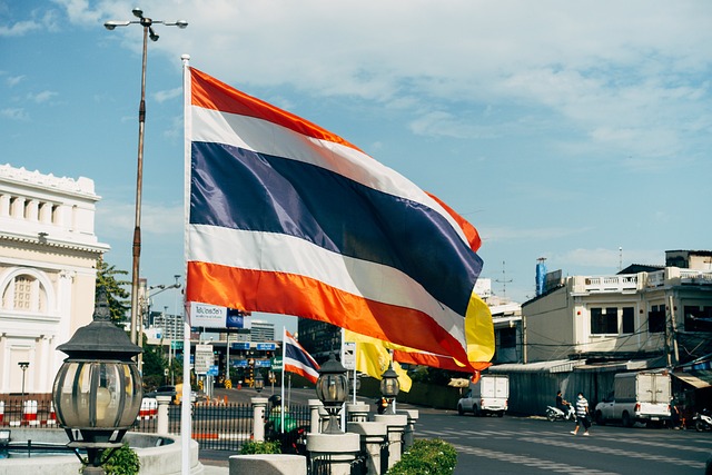 Thailand „Thailändische Flagge in Bangkok, wehend im Wind vor Gebäuden und blauem Himmel